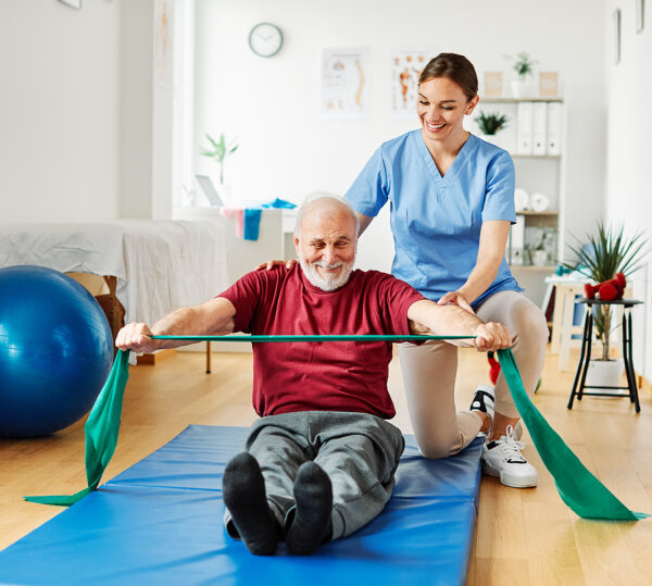 Caregiver Exercise With Senior Man At Clinic Or