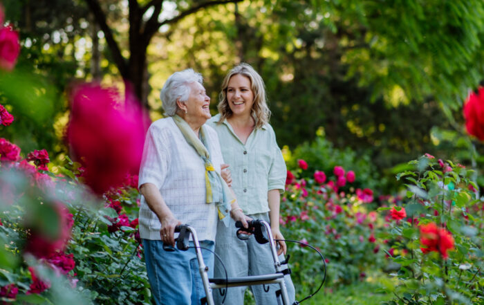 Adult supporting senior grandmother when taking her for walk with walker in park in summer.