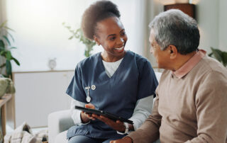 A caregiver holding a tablet smiles at an elderly man