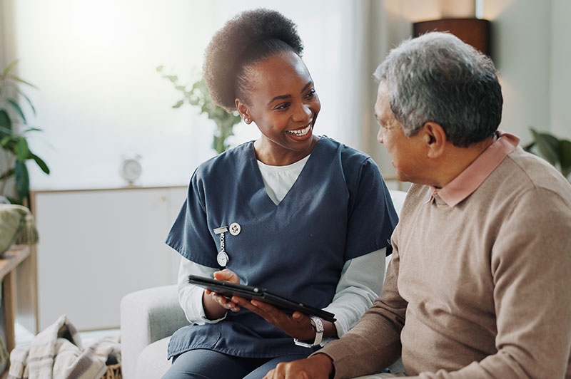 A caregiver holding a tablet smiles at an elderly man